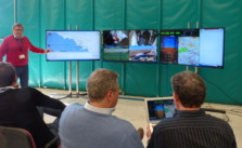 Männer verfolgen Testflüge/ Simulationen von Flugzeug-Drohnen im EU-Projekt RAID auf dem Monitor.