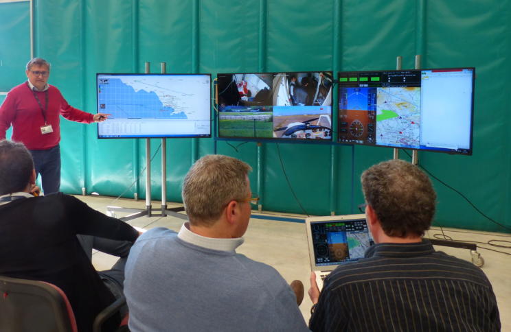 Männer verfolgen Testflüge/ Simulationen von Flugzeug-Drohnen im EU-Projekt RAID auf dem Monitor.