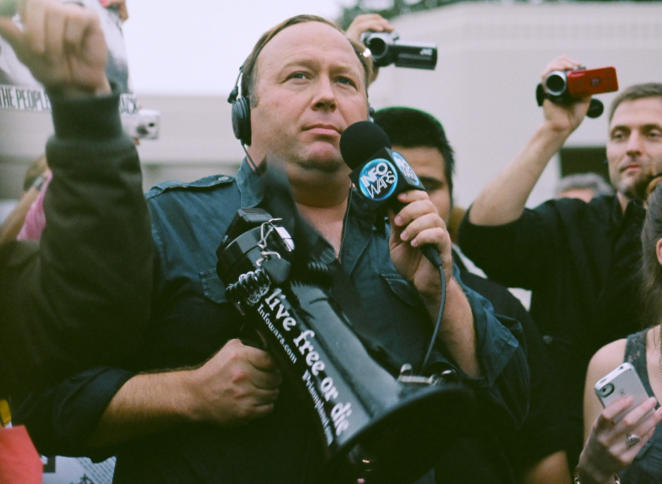 Alex Jones mit einem Megaphon in der rechten und einem Mikrophon in der linken Hand