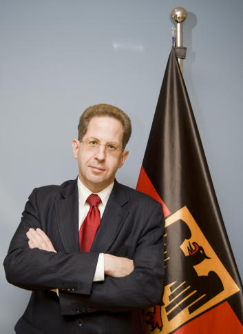 Hans-Georg Maaßen mit gekreuten Armen vor der Deutschlandflagge