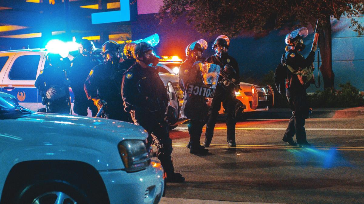 Auf einer dunklen straße stehen mehrere Polizisten vor Streifenwagen.
