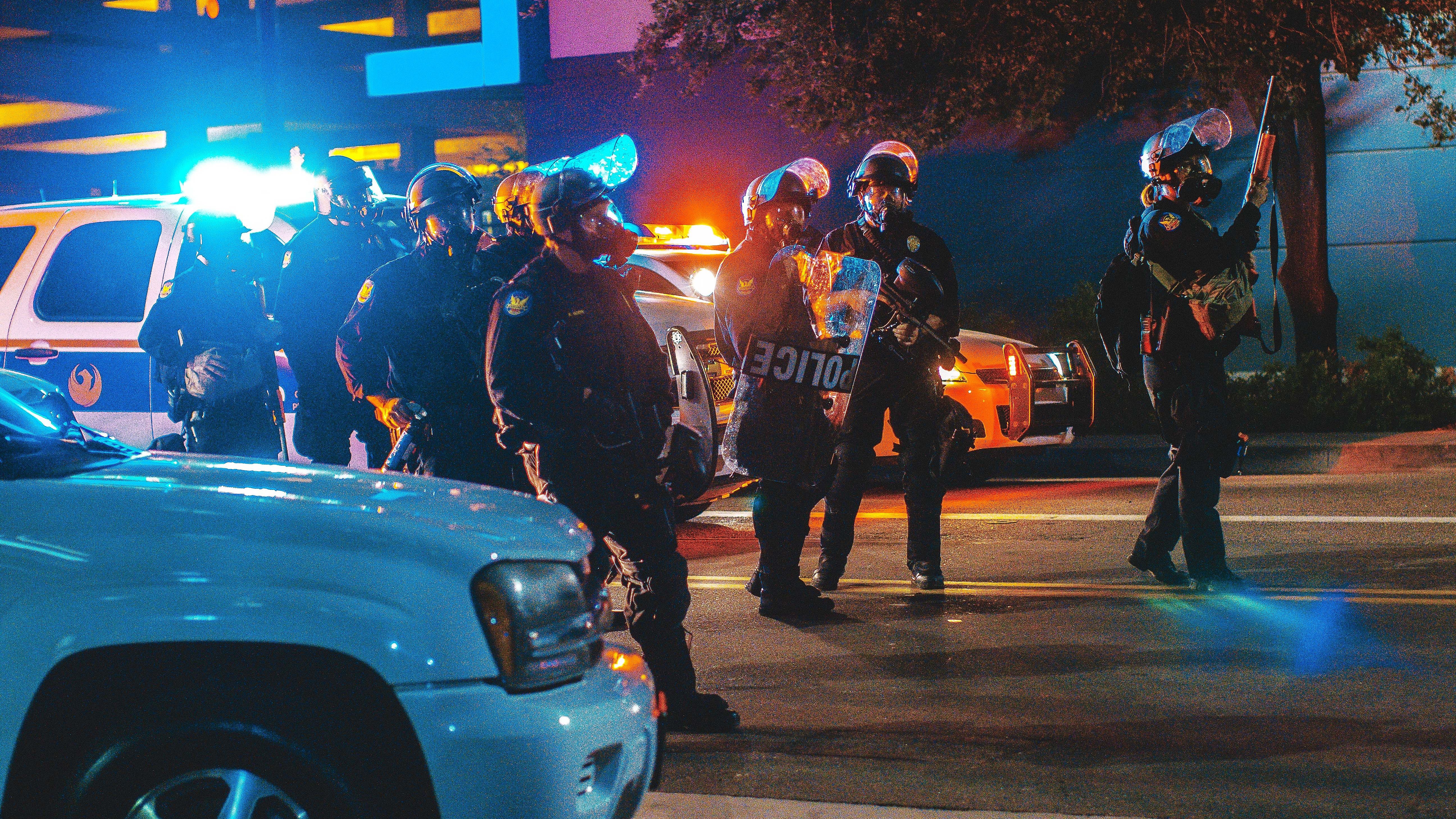 Auf einer dunklen straße stehen mehrere Polizisten vor Streifenwagen.