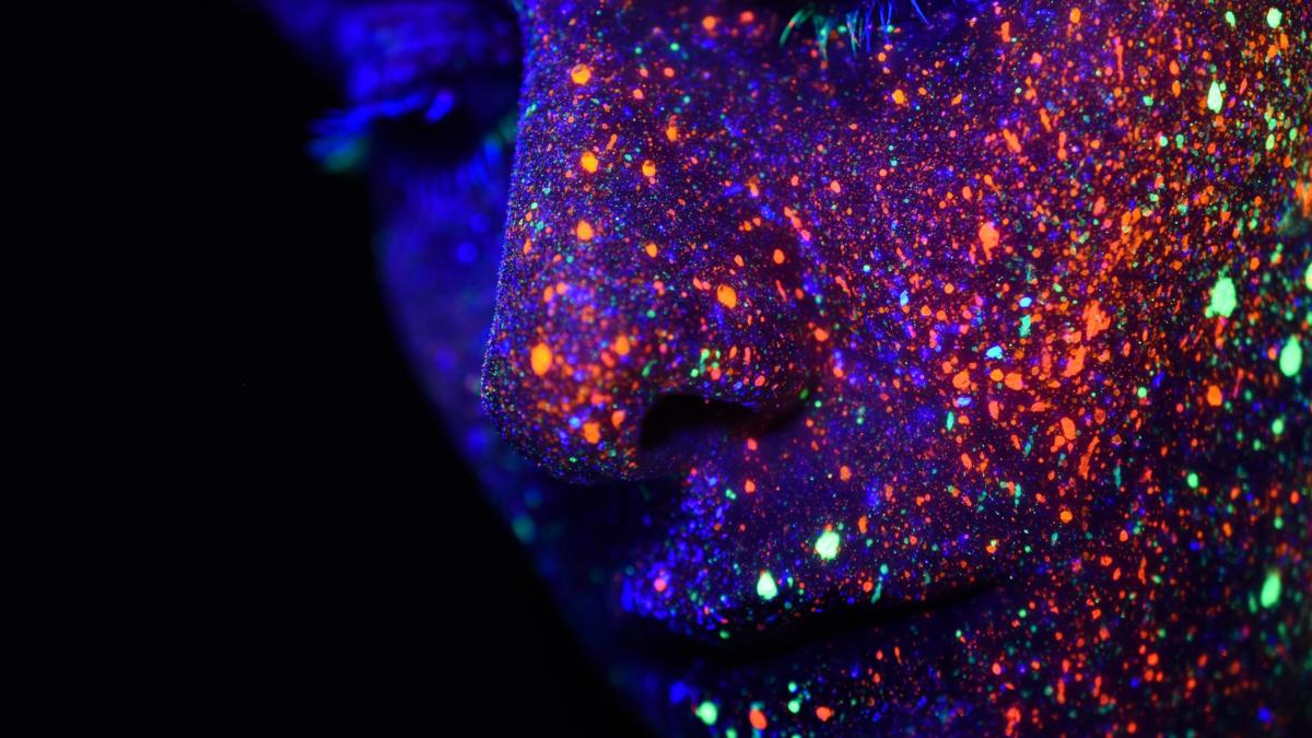 Gesenkter Blick eines Gesichts mit fluoreszierenden Farbspritzern.