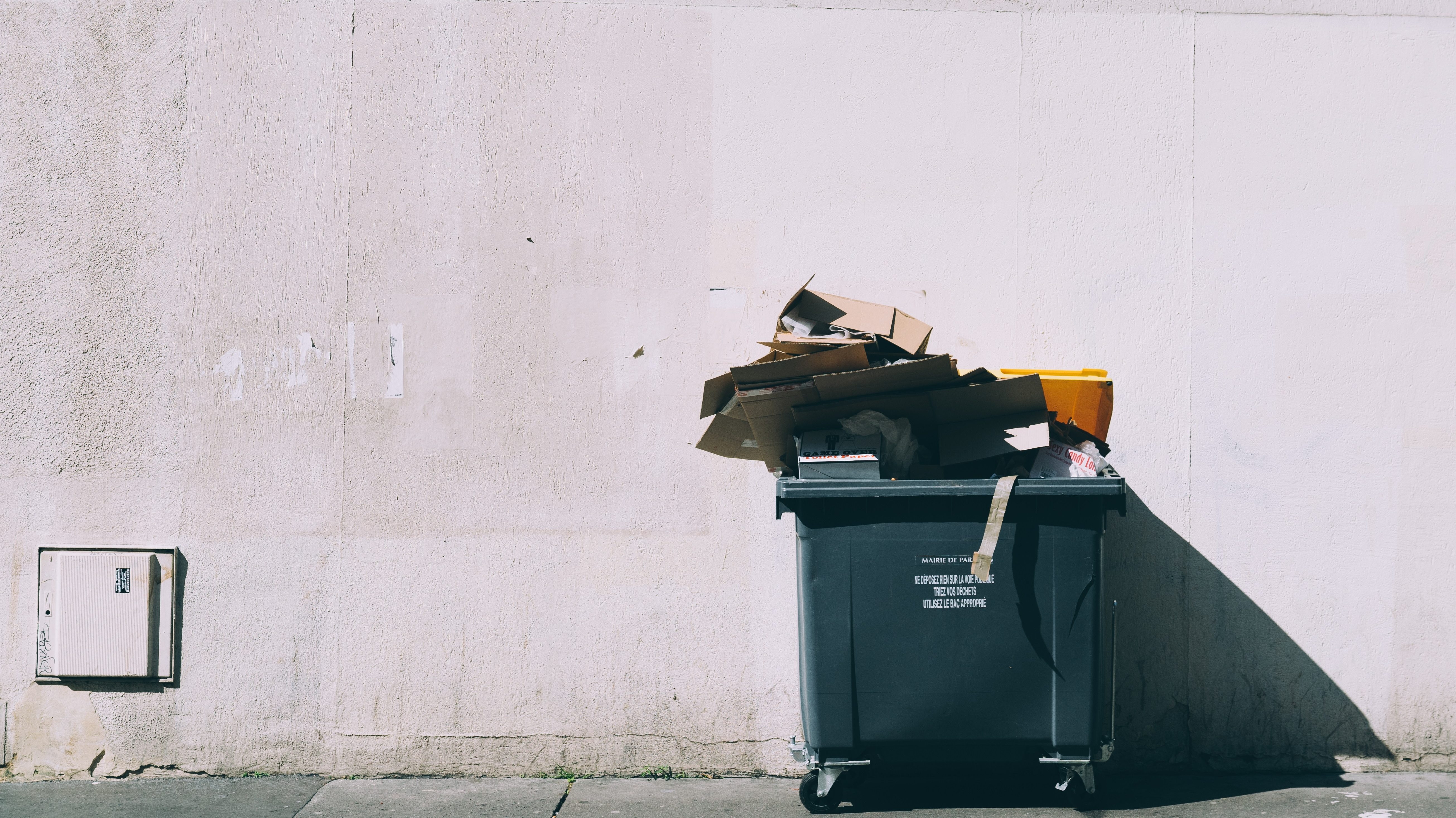 Ein schwarzer Müllcontainer vor einer grauen Wand.
