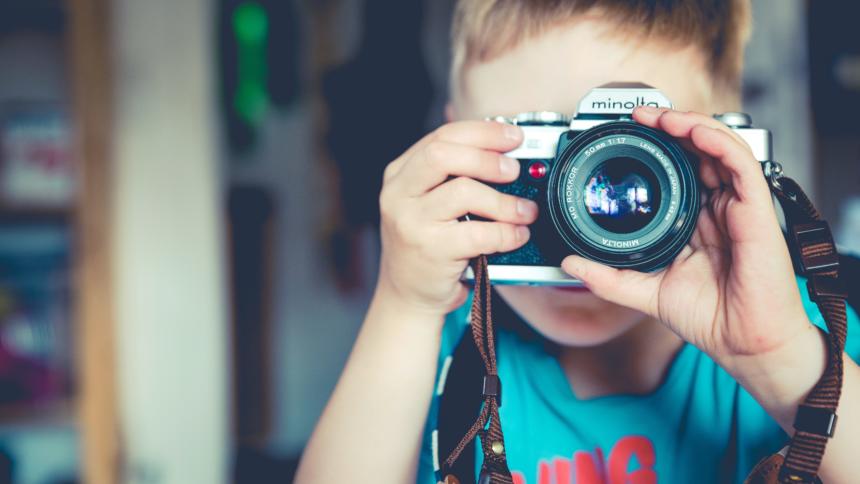 Ein Kind mit einer analogen Kamera vor dem Gesicht.