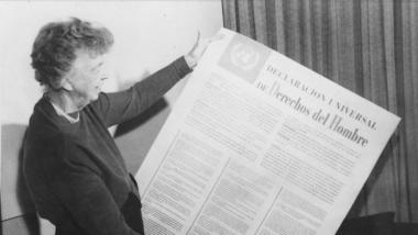 Ein schwarz-weißes Foto zeigt Eleanor Roosevelt, wie sie ein großes Blatt mit der Erklärung der Menschenrechte hält