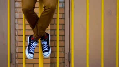 Eine Person sitzt auf einem gelben Gitter, braune Hose und schwerz/weiße Turnschuhe