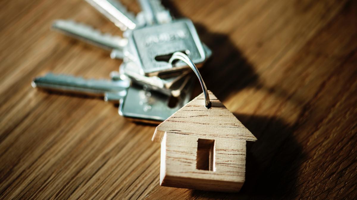 Ein Schlüsselbung mit einem Anhänger aus Holz, der ein Haus darstellt, auf einem hölzernen Untergrund