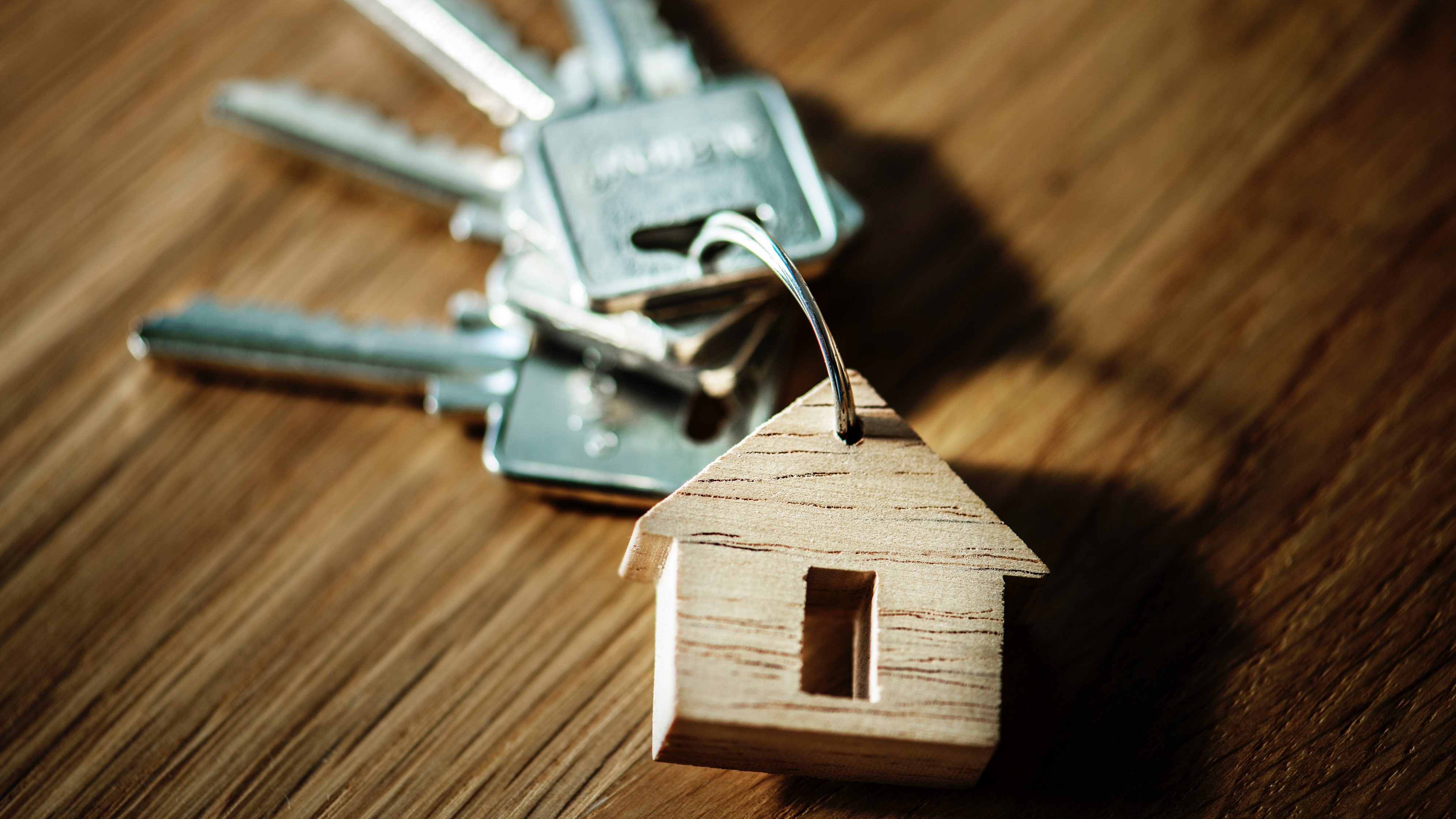 Ein Schlüsselbung mit einem Anhänger aus Holz, der ein Haus darstellt, auf einem hölzernen Untergrund