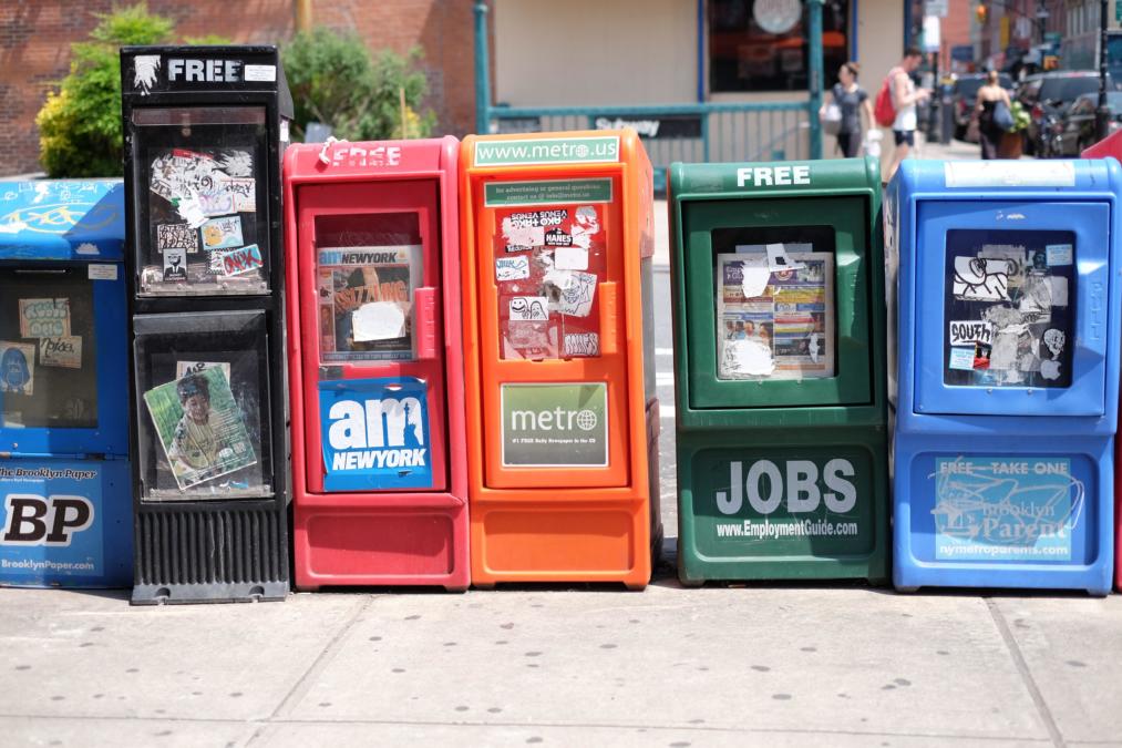 Aufgereihte Straßenzeitungsverkaufscontainer in unterschiedlichen Farben.