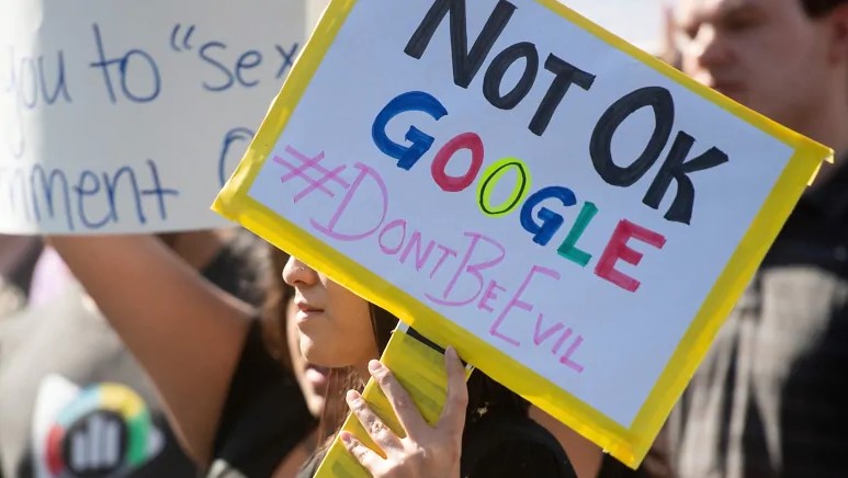 Frau hält Schild hoch, auf dem steht Not Okay Google