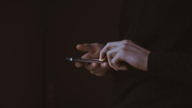 Hände halten ein Smartphone vor dunklem Hintergrund