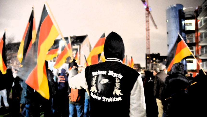Deutschlandfahnen, im Vordergrund ein Rechtsradikaler mit Nazi-Pullover