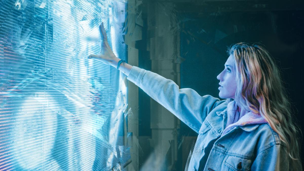 Eine junge Frau steht vor einer blau leuchtenden Kunstinstallation und streckt ihren Arm danach aus.