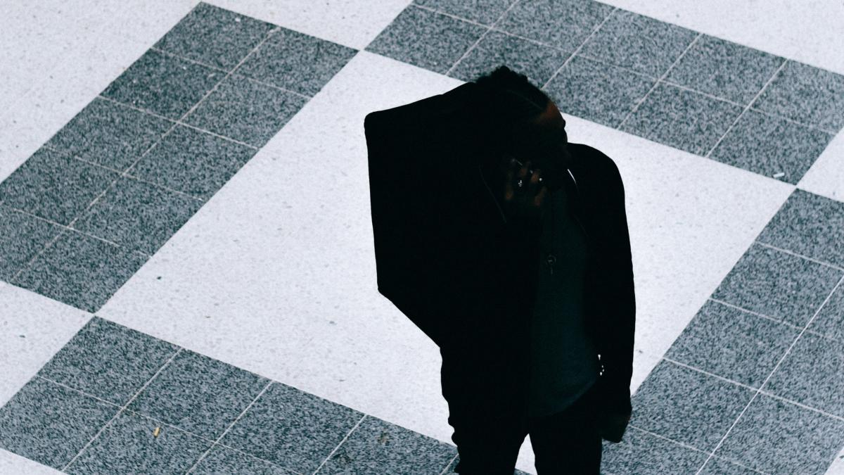 Die schwarze Silhouette eines abgestiegenen Deliveroo-Fahrers auf schwarz-weißem Kachelboden