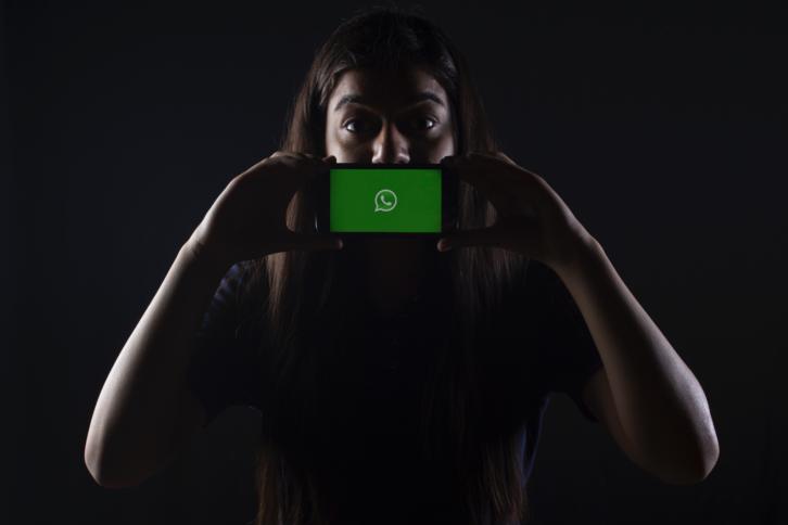 Ein Frau hält sich ein Smartphone mit dem WhatsApp-Logo vor den Mund.