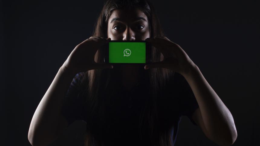 Ein Frau hält sich ein Smartphone mit dem WhatsApp-Logo vor den Mund.