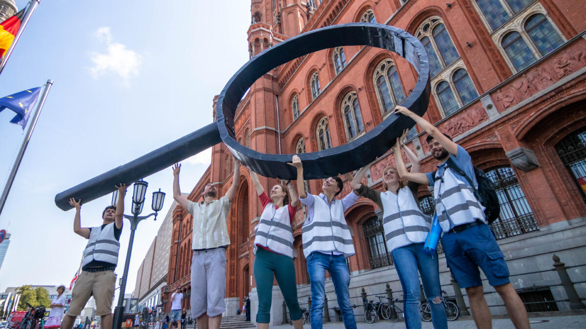 Mehrere Menschen halten vor dem Roten Rathaus eine überdimensionale Lupe hoch.