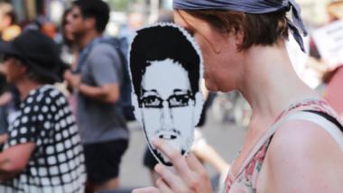 Demonstrantin hält ausgedrucktes Snowden-Gesicht