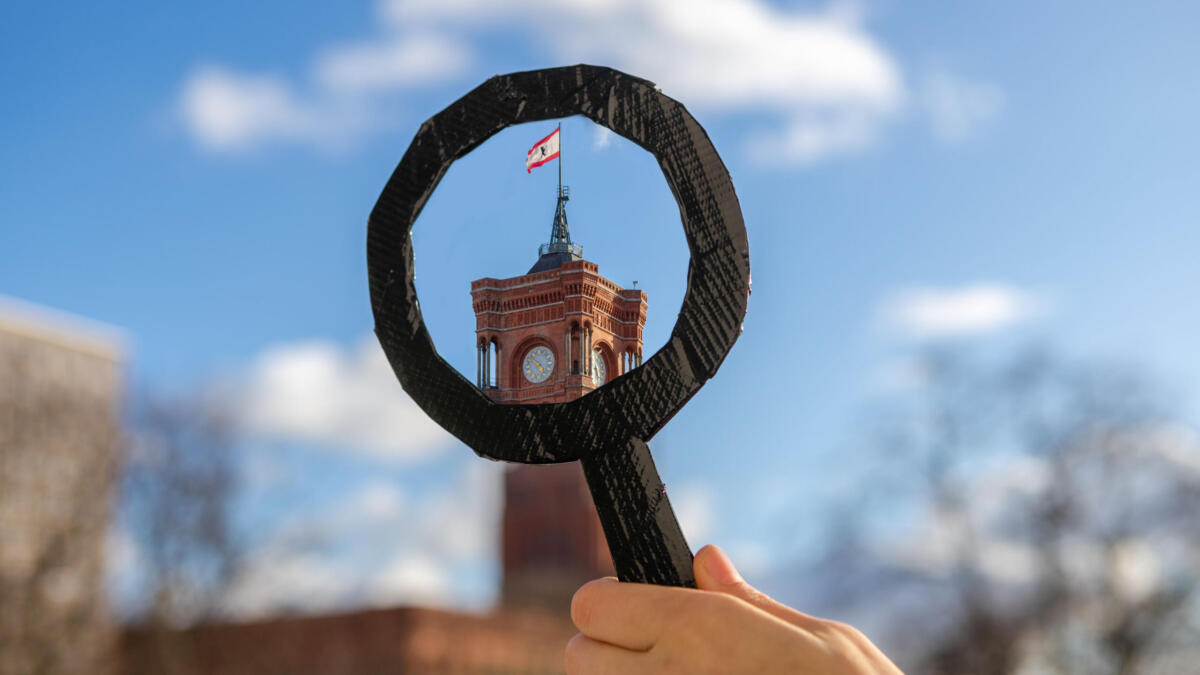 Jemand hält eine Lupe vpr das Rote Rathaus in Berlin