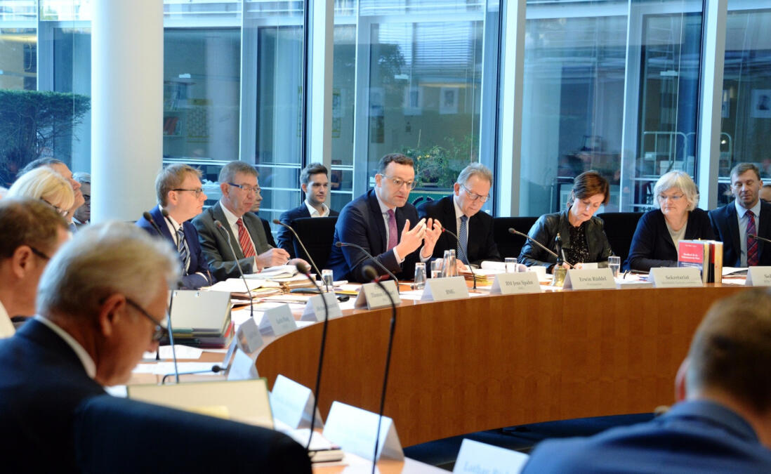 Jens Spahn gestikuliert vor dem Gesundheits-Ausschuss. Neben ihm sitzen weitere Politiker:innen.