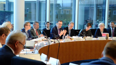 Jens Spahn gestikuliert vor dem Gesundheits-Ausschuss. Neben ihm sitzen weitere Politiker:innen.