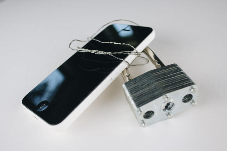 ein Smartphone, das mit Draht umwickelt ist. an dem draht ist ein vorhängeschluss befestigt.