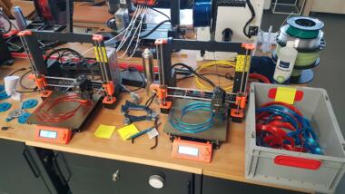 Eine Werkbank, auf der ein 3D-Drucker steht und viel Zubehör herumliegt.