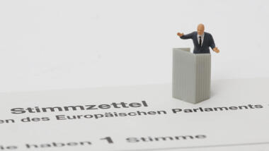 Eine kleine Figur eines Mannes im Anzug hinter einem Rednerpult steht auf einem Stimmzettel, der laut Aufschrift zu den EU-Wahlen gehört.