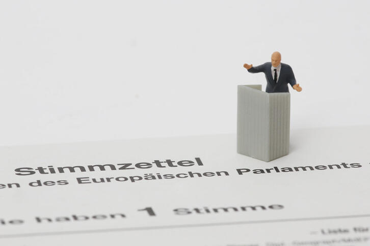 Eine kleine Figur eines Mannes im Anzug hinter einem Rednerpult steht auf einem Stimmzettel, der laut Aufschrift zu den EU-Wahlen gehört.