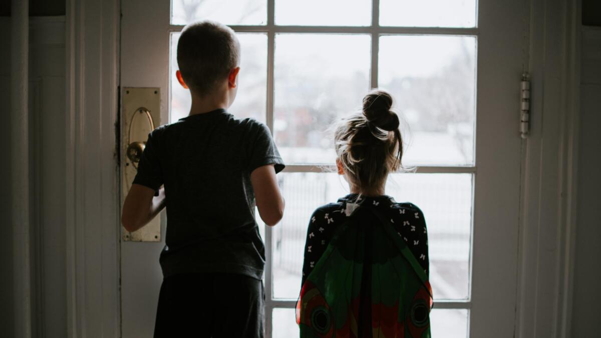 Junge und Mädchen stehen vor geschlossener Tür und schauen nach draußen.