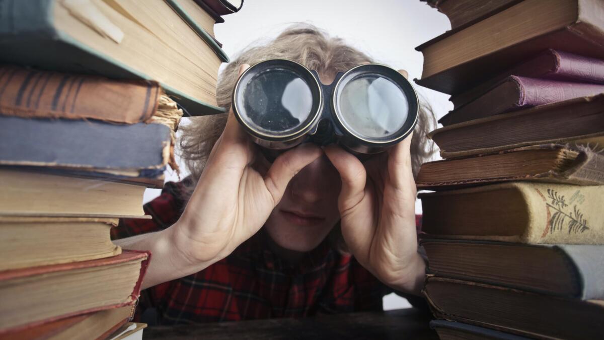 Person mit Fernglas zwischen zwei Bücherstapeln