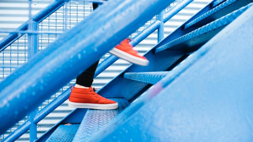 Blaue Treppe mit Füßen in roten Schuhen, die nach oben gehen.