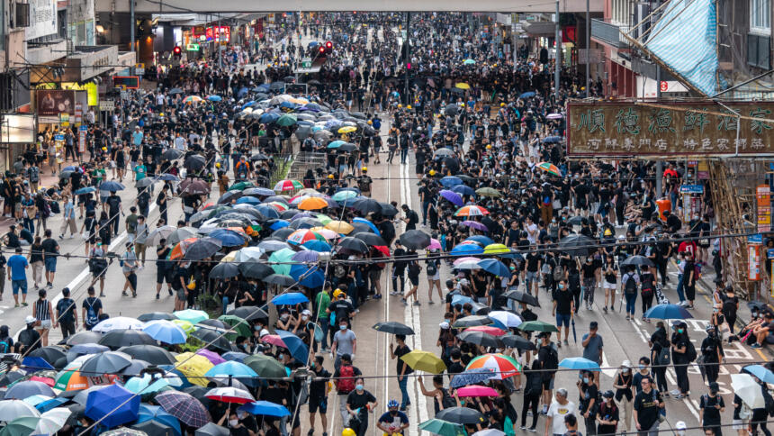 Demonstrant:innen sammeln sich mit Regenschirmen in Hongkongs Straßen.