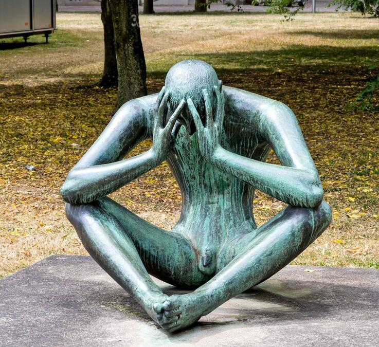 Skulptur "Der Denker": Eine Person sitzt auf dem Boden und hat das Gesicht in den Händen verborgen.