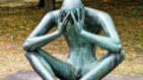 Skulptur "Der Denker": Eine Person sitzt auf dem Boden und hat das Gesicht in den Händen verborgen.