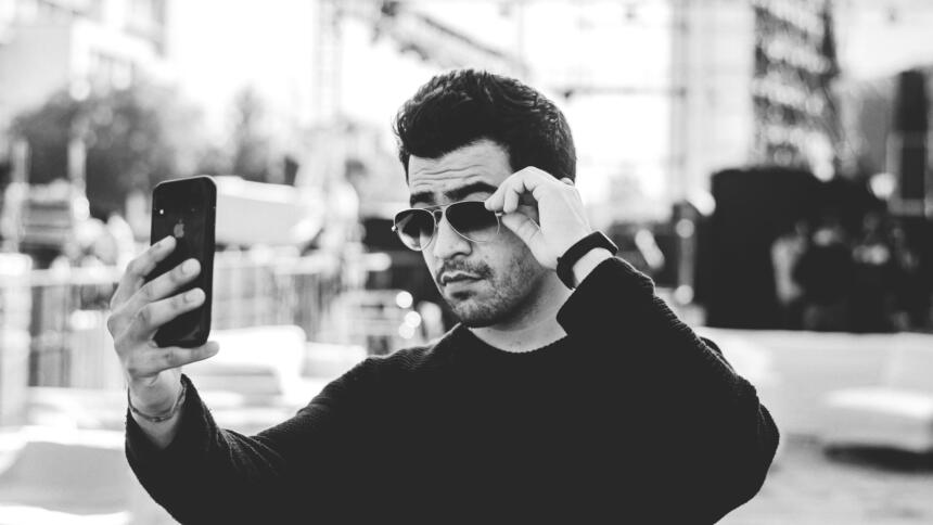 Mann mit Sonnenbrille fotografiert sich mit handy