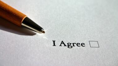 Ein Stift liegt auf einem Blatt Papier mit einem Kästchen, neben dem "I Agree" steht.
