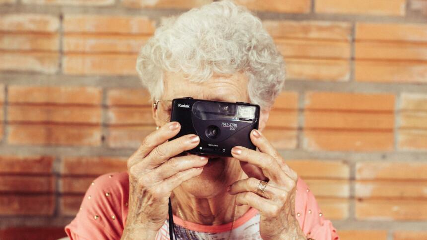 Eine Frau mit grauen Haaren schaut durch den Sucher einer Kamera.