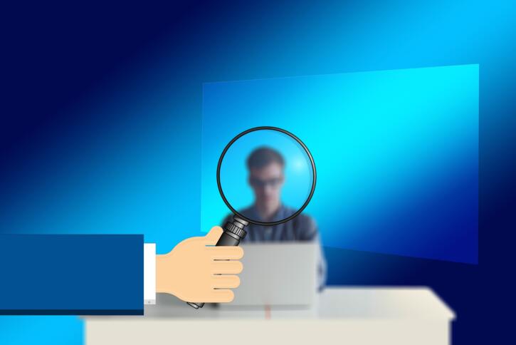 Eine Lupe zeigt eine verschwommene Figur, die vor einem Computer sitzt.