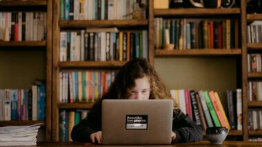 Kind am Laptop vor Bücherwand