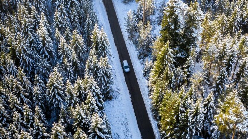 Vogelperspektive: Ein Auto fährt in einem verschneiten Wald auf einer geraden Straße