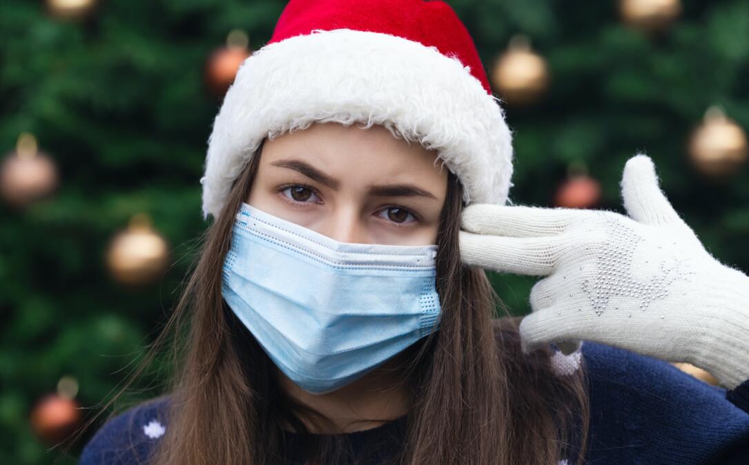 Frau mit Weihnachtsmannmütze und Mundschutz hält sich Finger an den Kopf