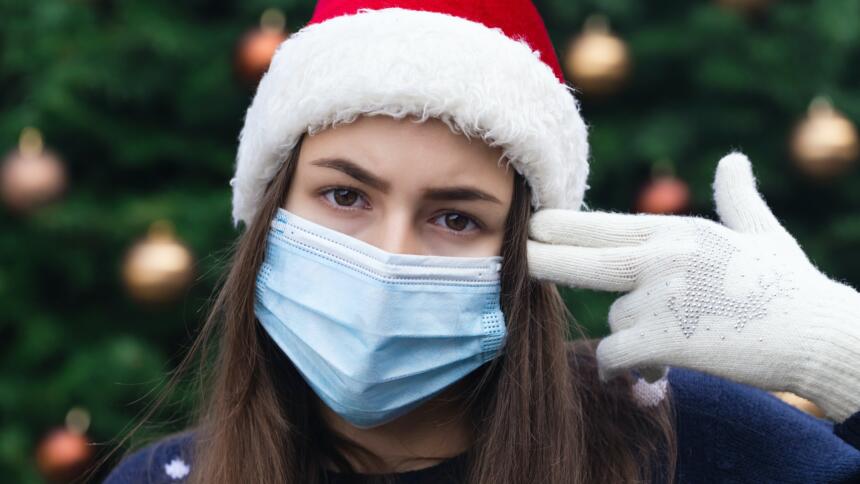 Frau mit Weihnachtsmannmütze und Mundschutz hält sich Finger an den Kopf