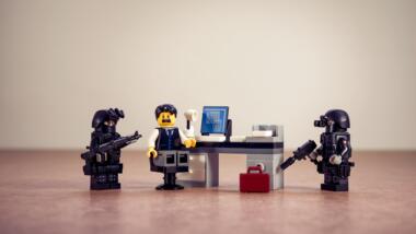 Zwei Lego-Polizisten umringen einen Lego-Behördenmitarbeiter, der ängstlich schaut.