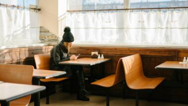 Person sitzt in einem leeren Restaurant und schaut auf Handy