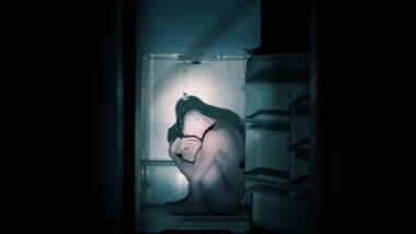Nackter Mensch sitzt in einem Kühlschrank