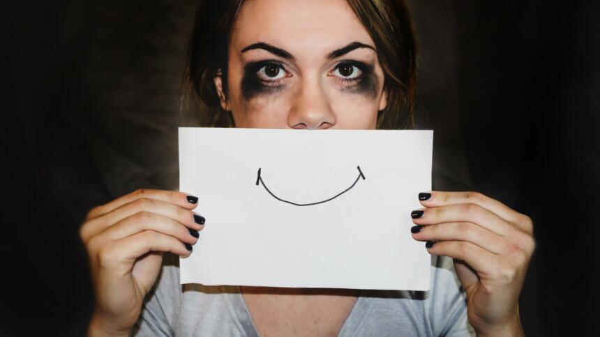 Ein Smiley auf Papier vor einem traurigen Augenpaar