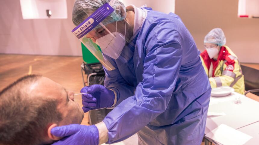 Medizinisches Personal in Schutzkleidung nimmt bei einem Patienten einen Nasenabstrich.