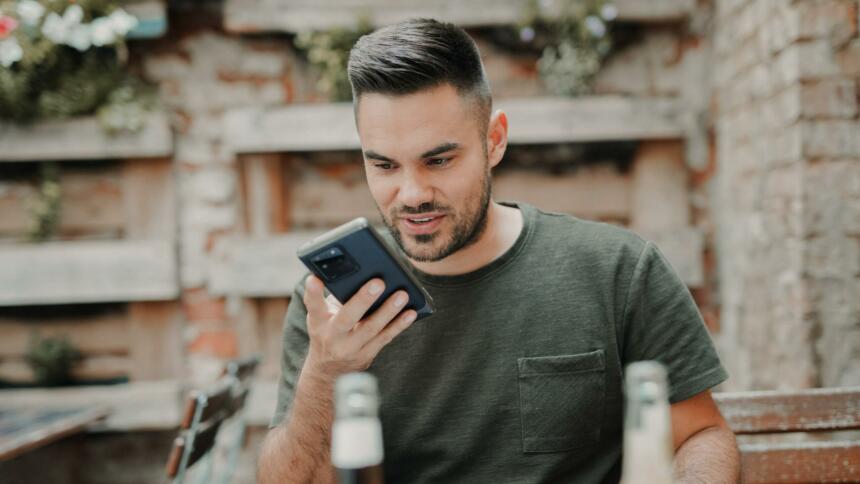 Mann sitzt im Biergarten und schaut aufs Handy